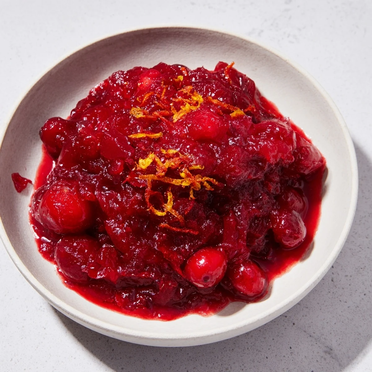 Close-up of bubbling cranberry sauce with ginger, showing a glossy texture and bursting berries.
