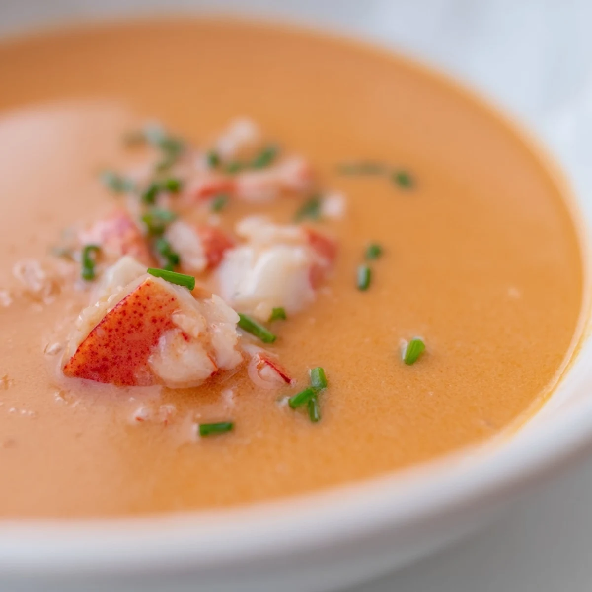 Close-up of Creamy Lobster Bisque showcasing the smooth, warm orange broth and tender pieces of lobster meat, ready to be enjoyed.