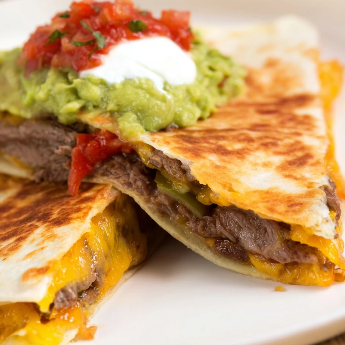 Freshly made Tex-Mex Beef Quesadillas oozing melted cheese with salsa and guacamole.