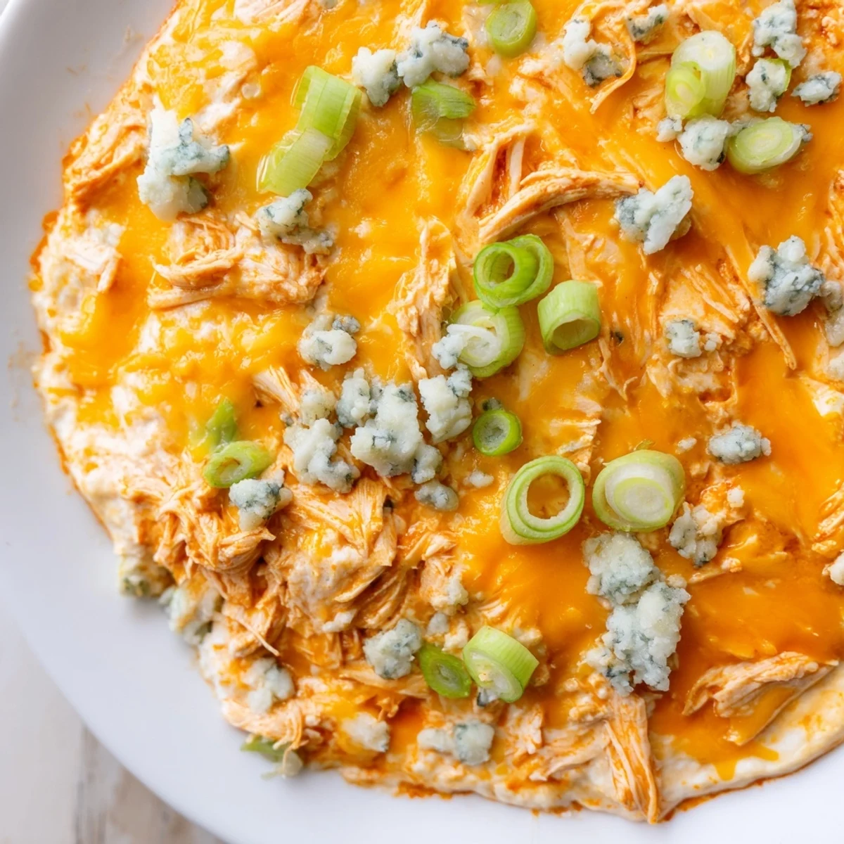 A steaming dish of Spicy Buffalo Chicken Dip with shredded chicken, blue cheese crumbles, and dippers on the side.