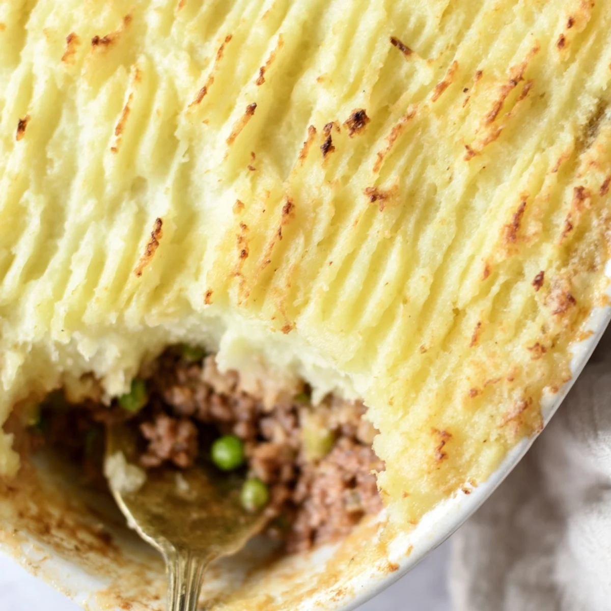 Close-up of a serving of Beef Shepherds Pie with Peas on a plate, garnished with fresh thyme and ready to enjoy with a glass of red wine.