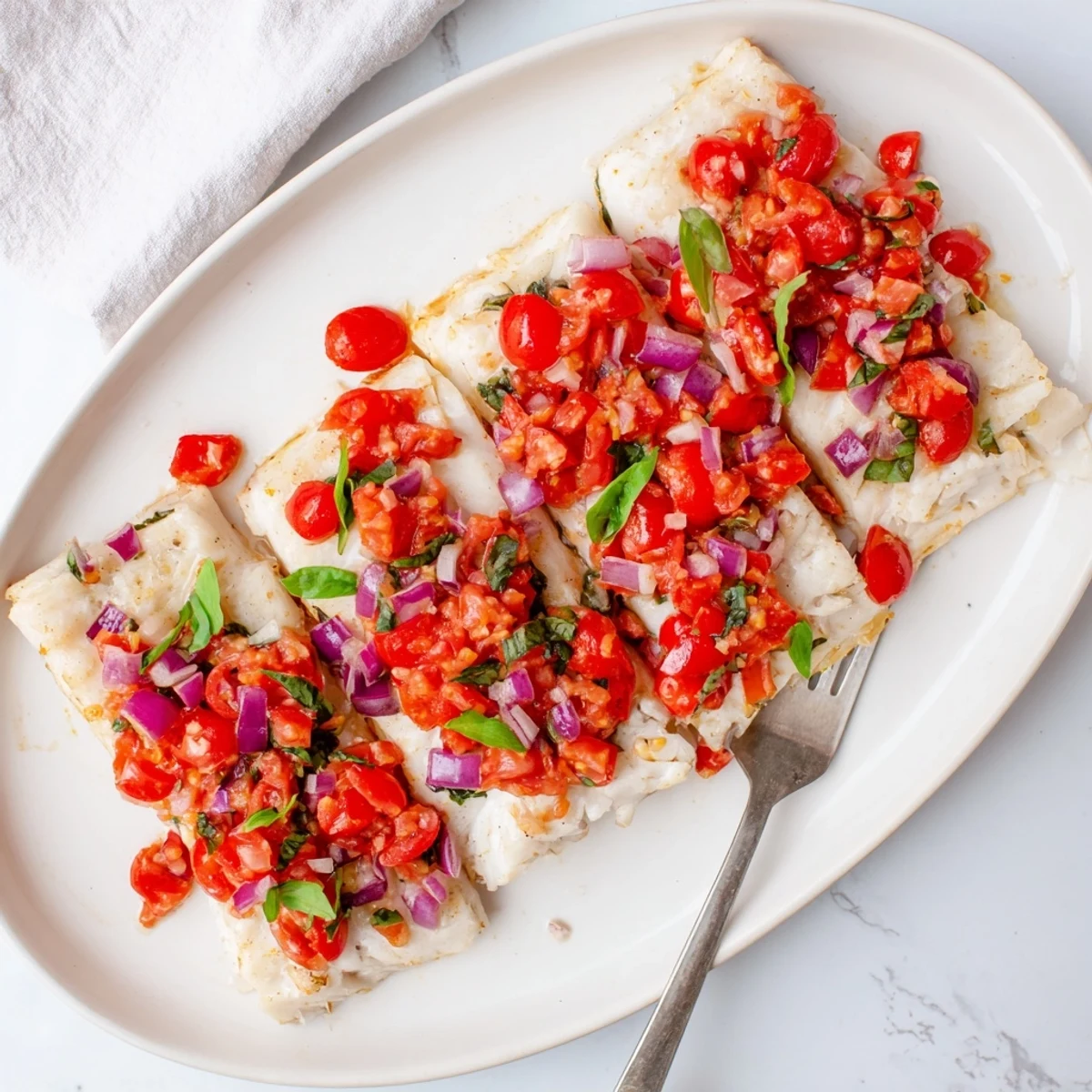 Golden-brown baked halibut fillets topped with a fresh, vibrant tomato and basil relish, served on a white plate.  