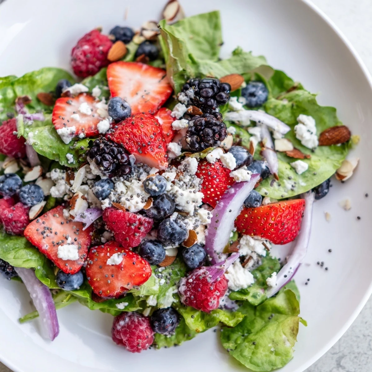 Close-up of a Berry Salad with Poppy Seed Dressing topped with raspberries, blackberries, toasted almonds, and thinly sliced red onion.