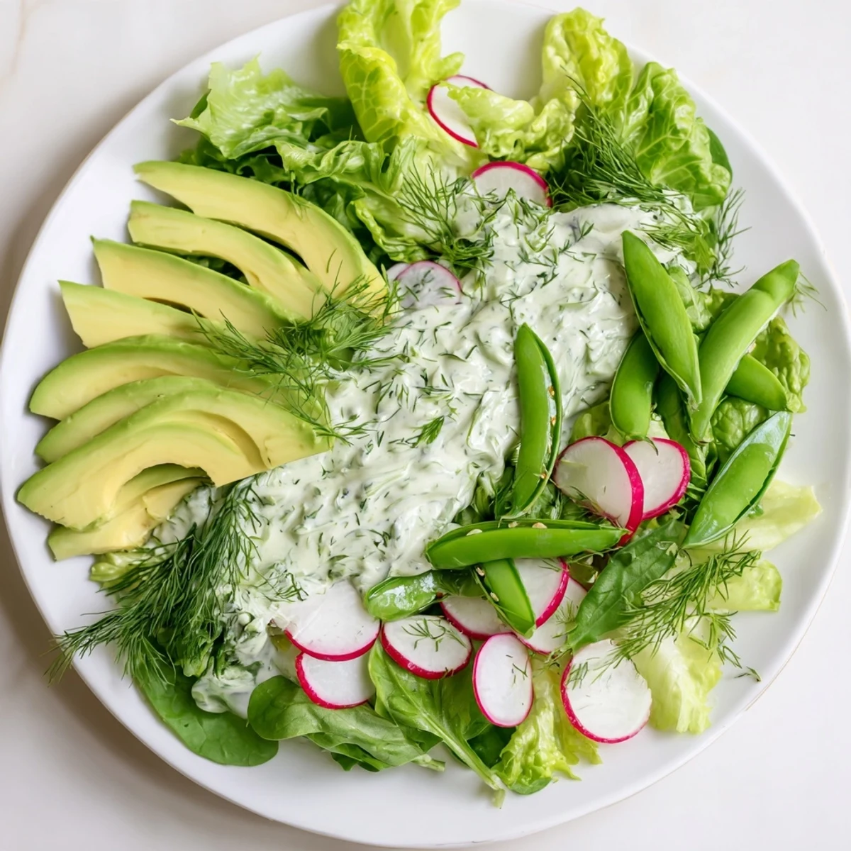 A vibrant bowl of Green Salad with Green Goddess Dressing, featuring crisp greens, cucumber, and radishes with creamy avocado slices.