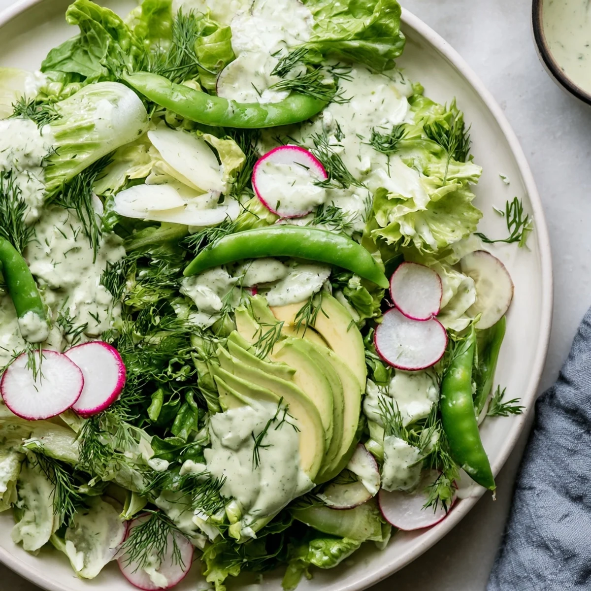 Plated Green Salad with Green Goddess Dressing with mixed greens, cucumber, and avocado, drizzled in a creamy dressing for a refreshing side.