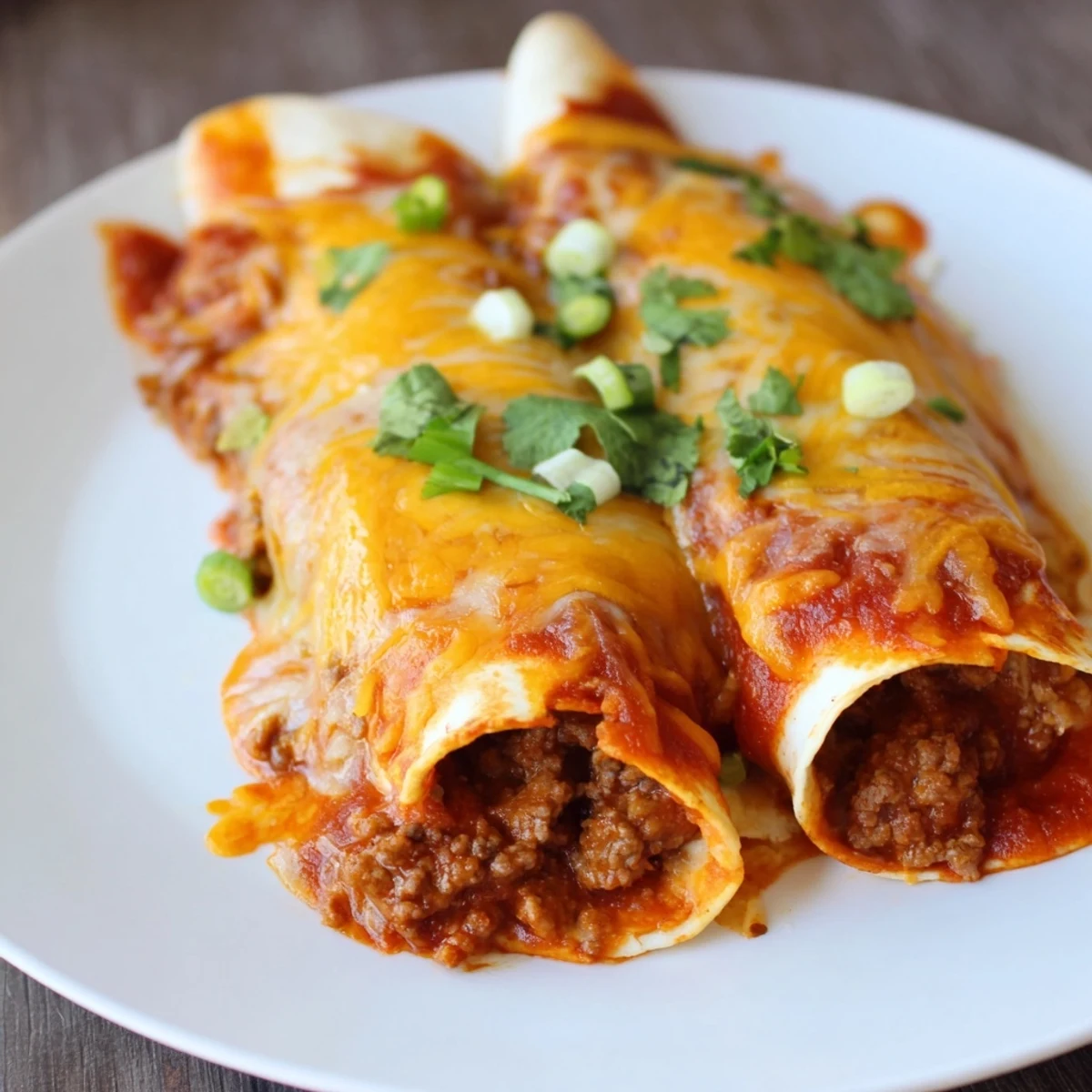 A serving platter holds Beef Enchiladas with Homemade Red Sauce, drizzled with extra sauce and green onions for garnish.