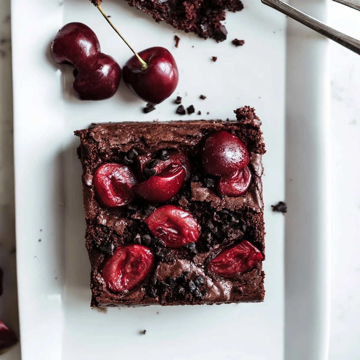Freshly roasted cherries top a square of fudgy Roasted Cherry Brownies on a white plate.