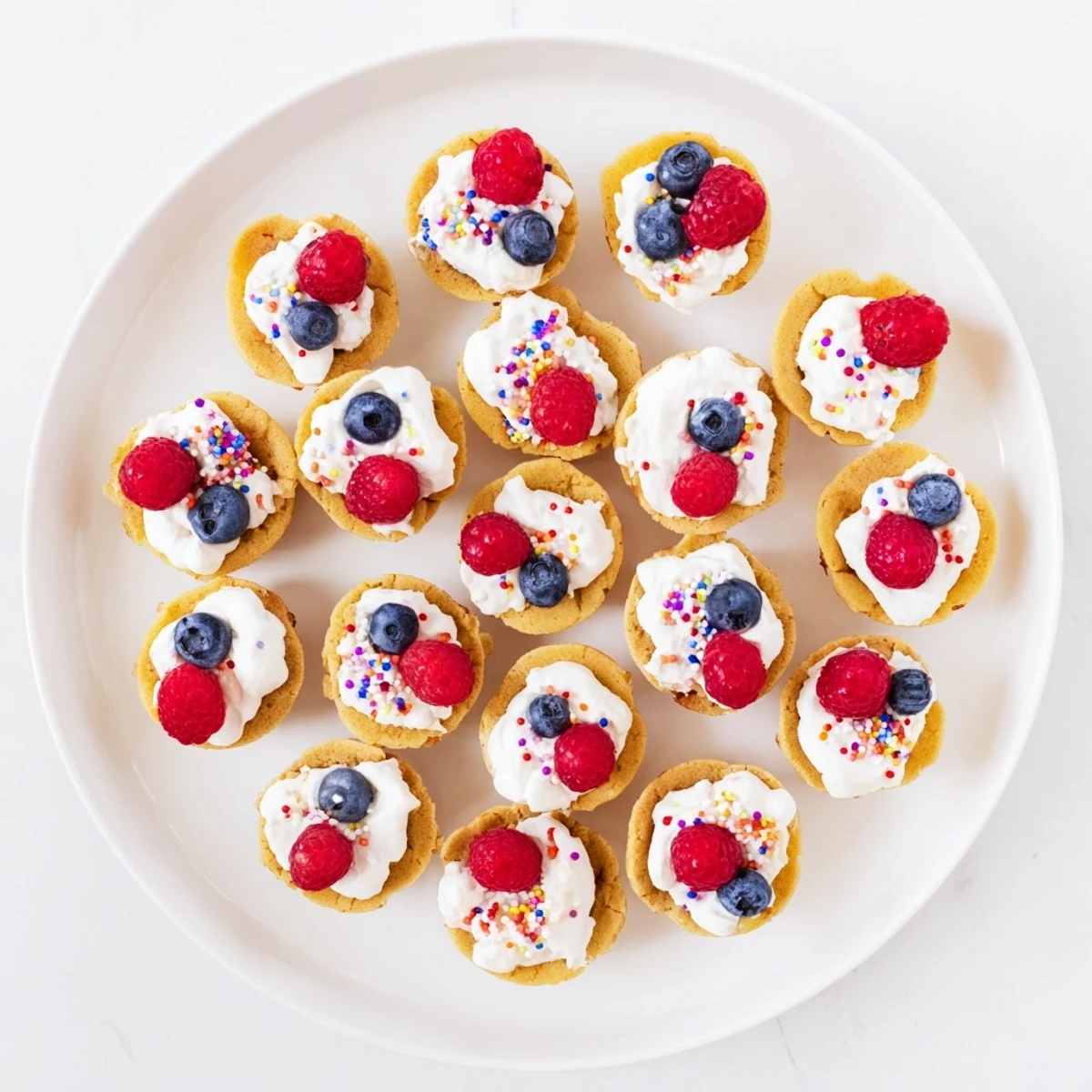 Sugar Cookie Cups displayed on a white plate topped with fresh raspberries, blueberries, and a light dusting of powdered sugar.