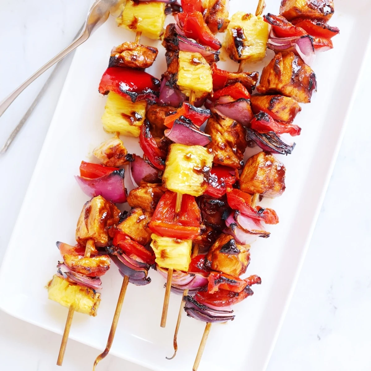 Smoky glazed Chicken and Pineapple BBQ Skewers paired with sweet pineapple chunks and crisp bell peppers on a platter.