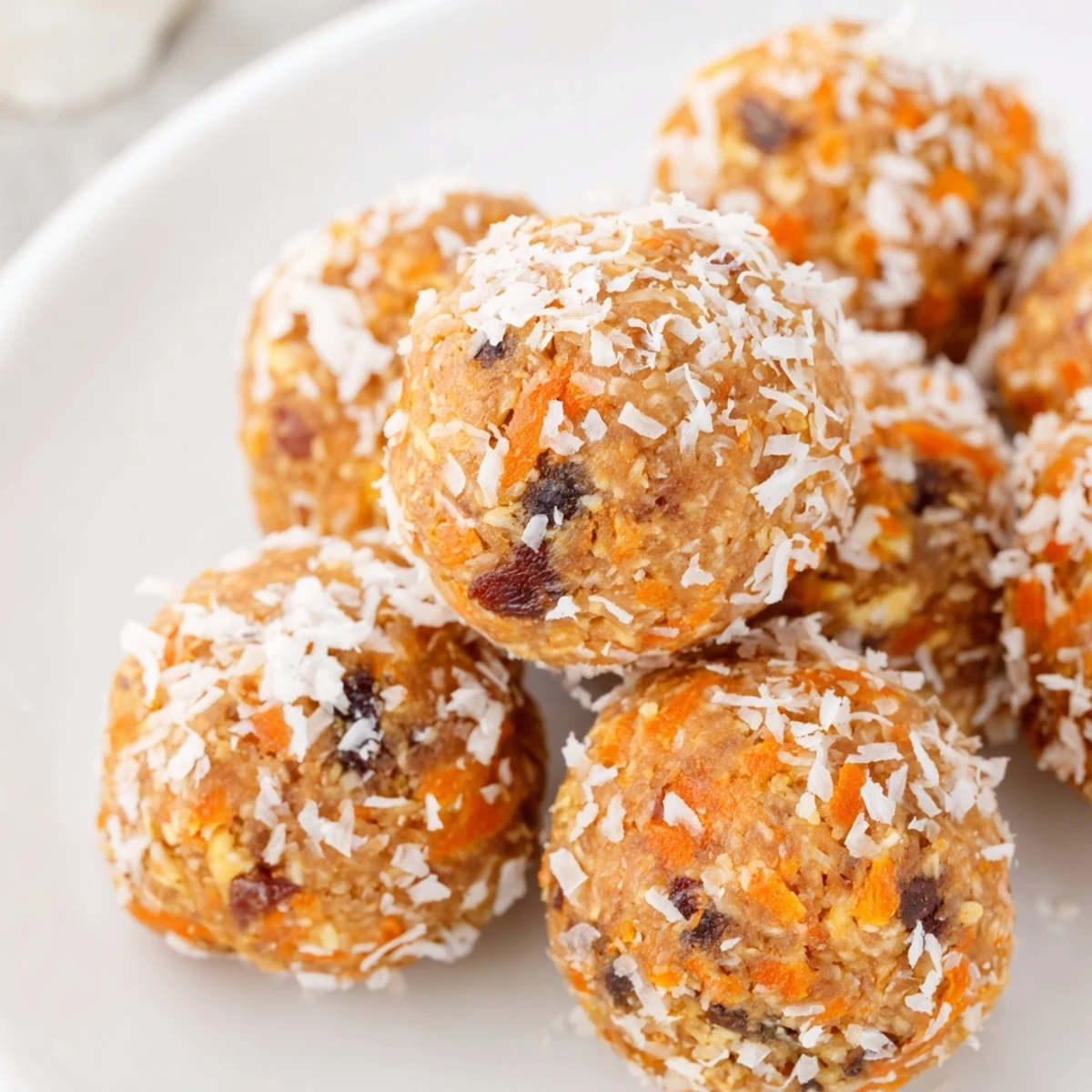 Vibrant orange No Bake Carrot Cake Bites coated in coconut, served alongside a glass of cold almond milk.