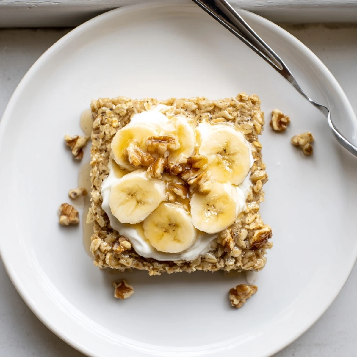A slice of warm Banana Baked Oatmeal on a plate, drizzled with maple syrup and chopped walnuts.
