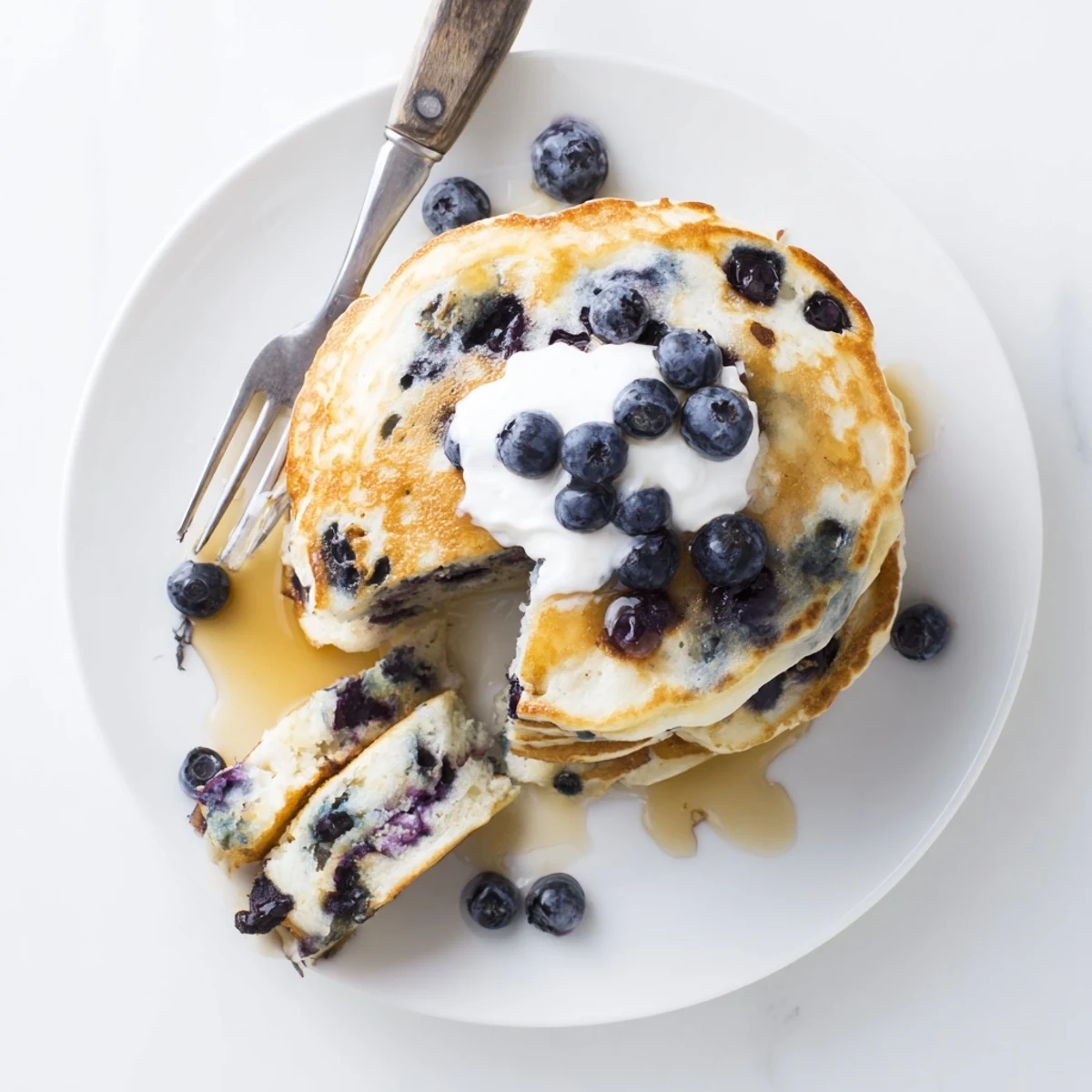 Freshly cooked Greek Yogurt Blueberry Pancakes served with yogurt dollop, extra blueberries, and warm maple syrup drizzle.