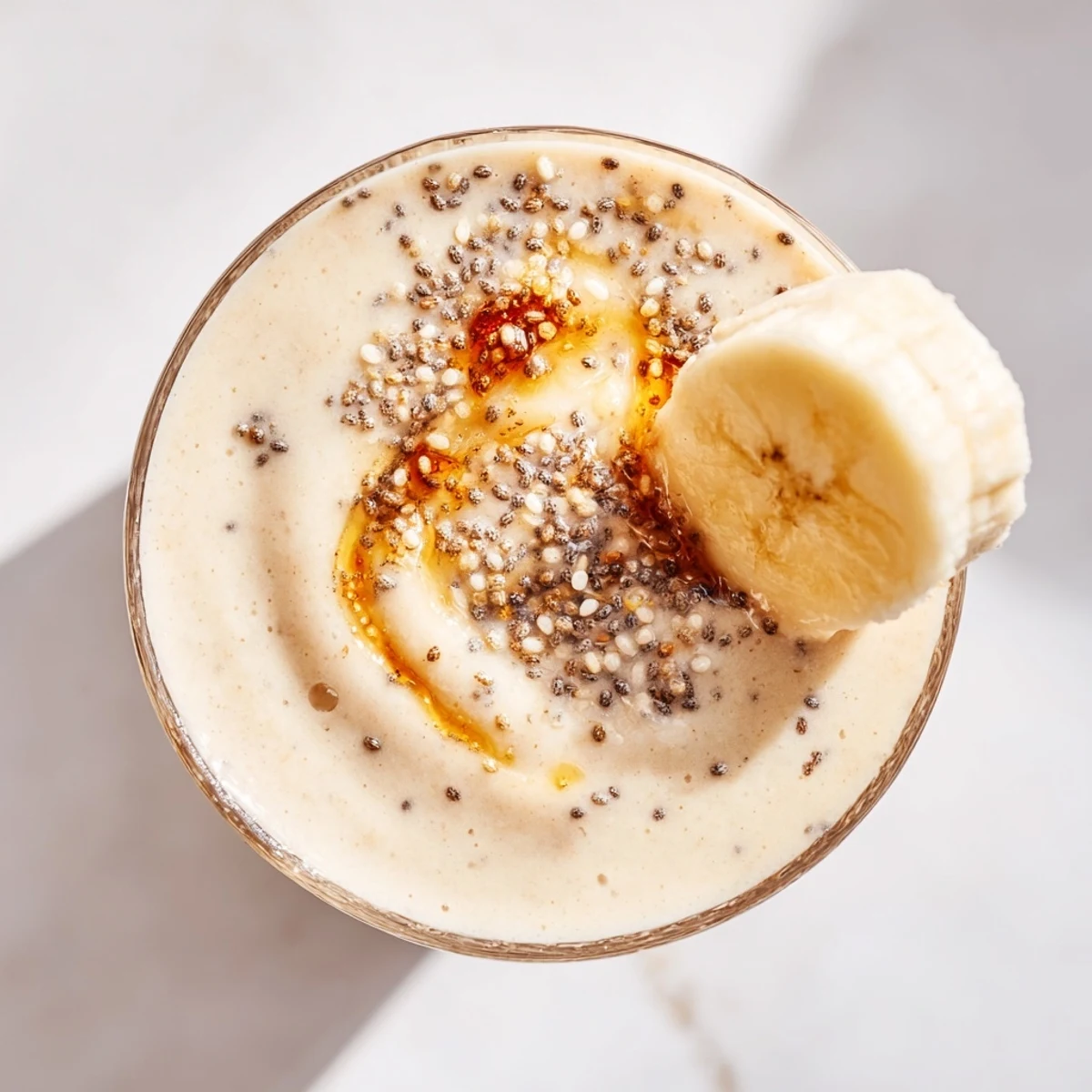 Thick blended Greek yogurt banana smoothie in clear glass with optional chia seeds and honey drizzle on rim