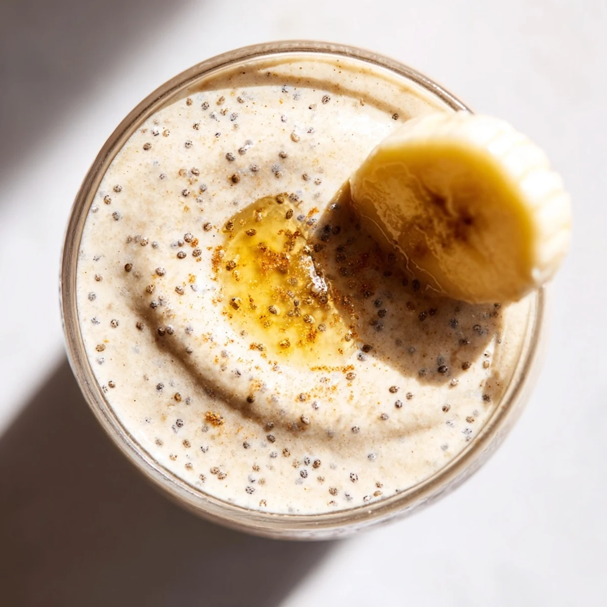 Golden yellow Greek yogurt banana smoothie garnished with banana rounds and granola for breakfast or snack time