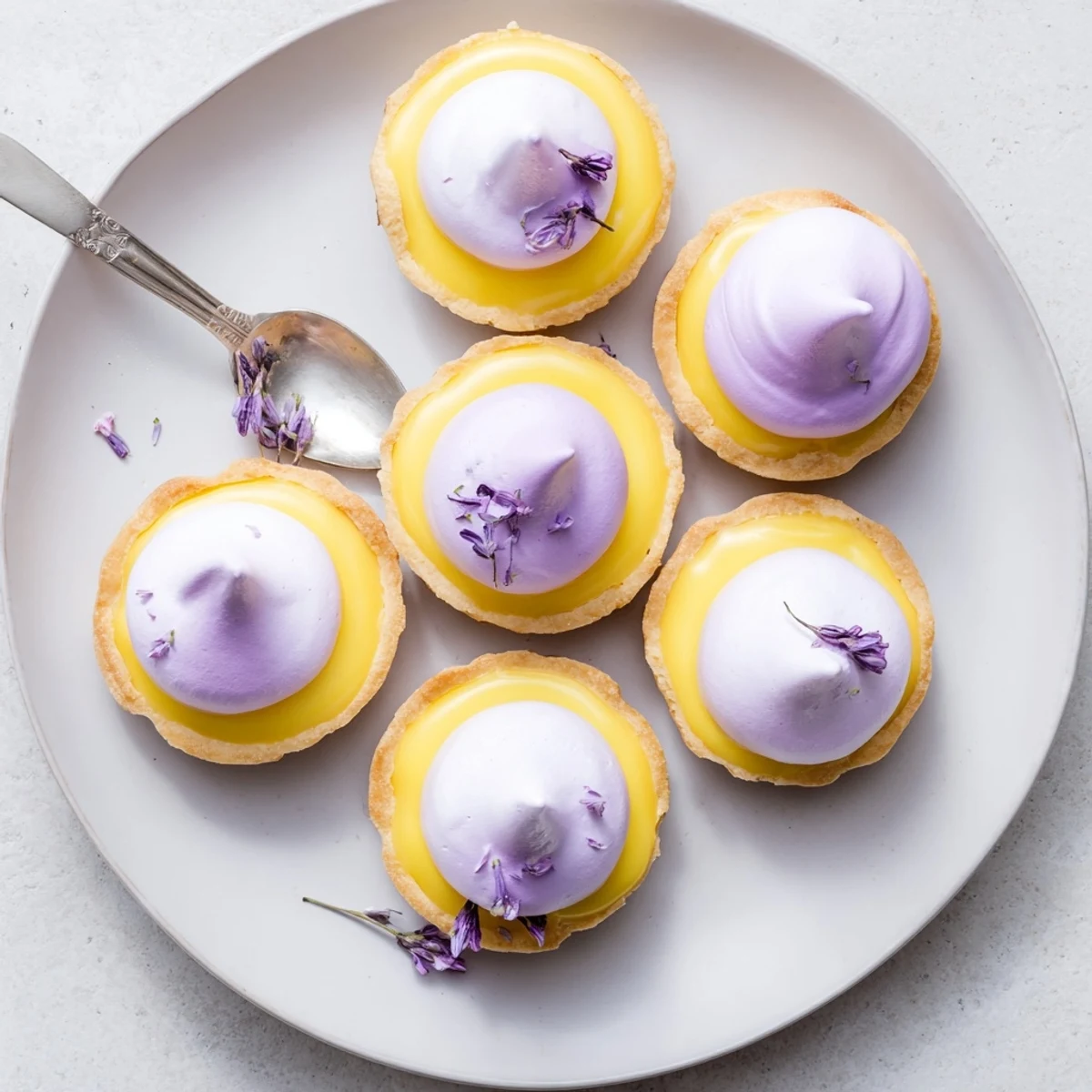 Elegant dessert table spread showcasing six mini lemon tarts with lightly charred lilac meringue swirls