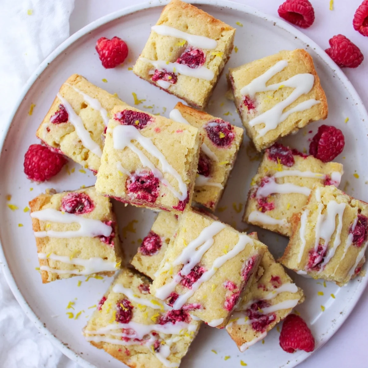 Square raspberry lemon blondies topped with tangy glaze and fresh raspberry garnish