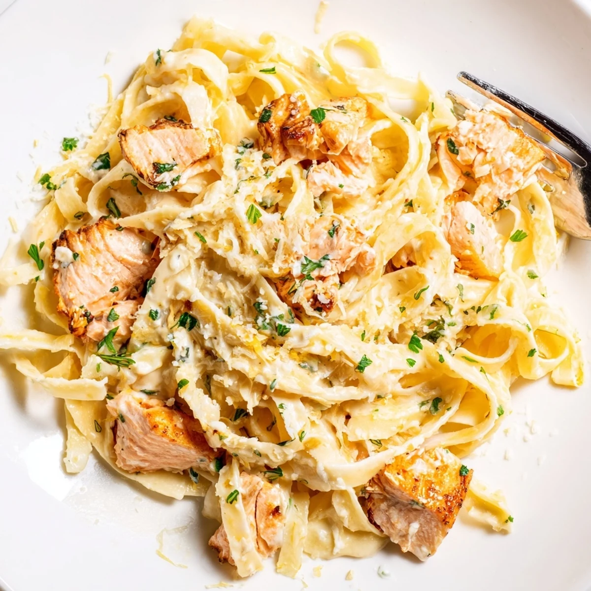 Golden seared salmon flakes resting on creamy garlic butter fettuccine with bright lemon and parsley garnish