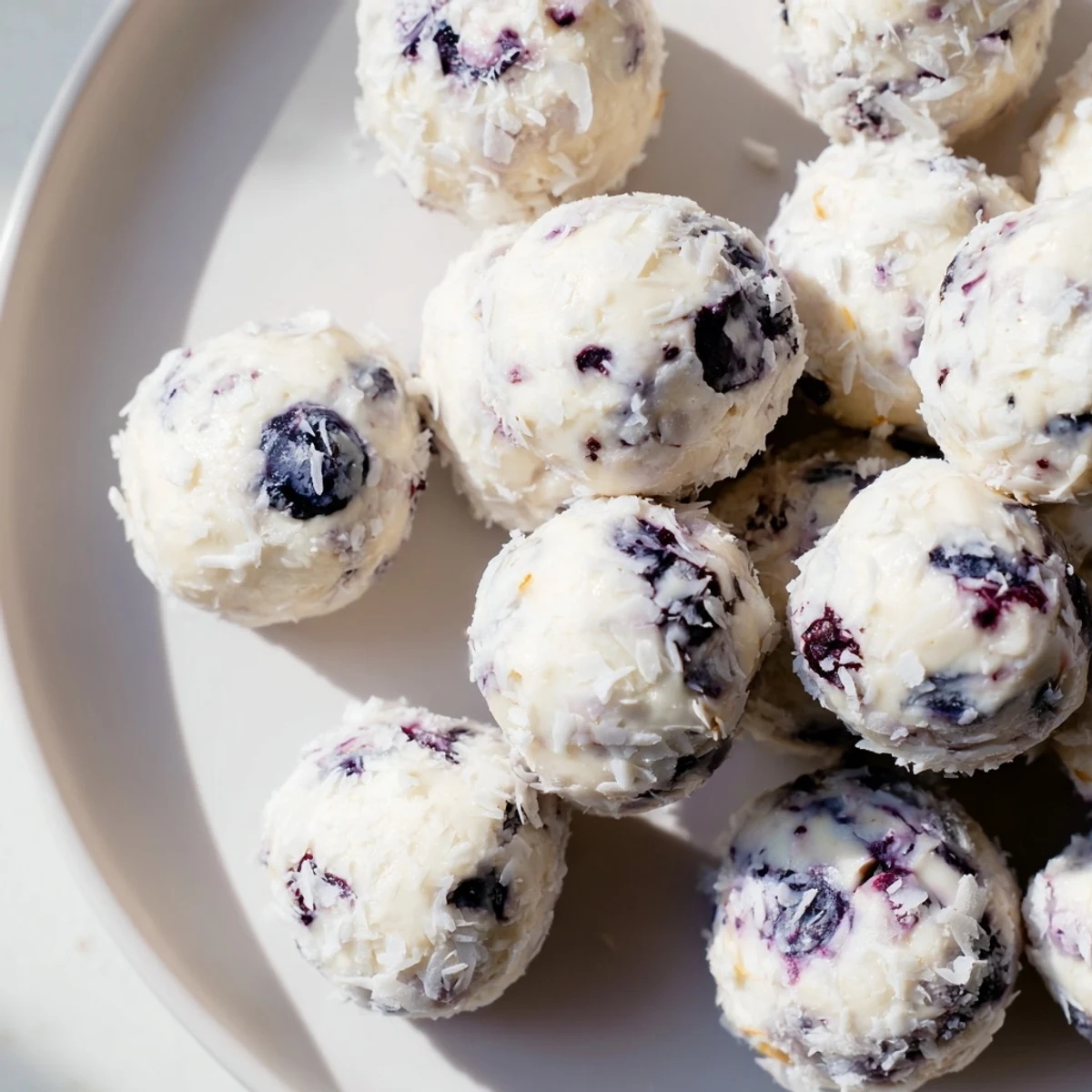 Bite-sized blueberry cheesecake protein bites topped with shredded coconut on a white plate