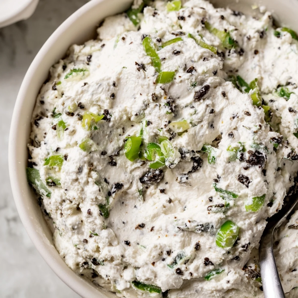 Cream cheese olive dip served in a white bowl with colorful chopped olives and green onion garnish