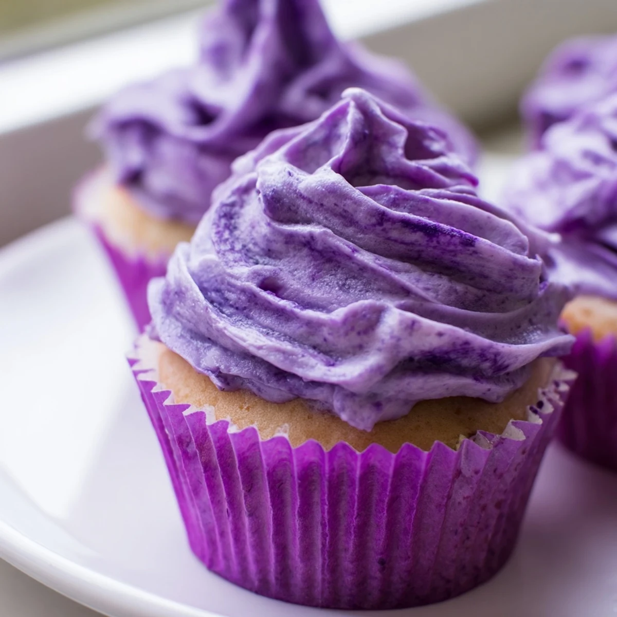 Fluffy purple Grape Soda cupcakes topped with swirls of grape buttercream frosting on a white plate
