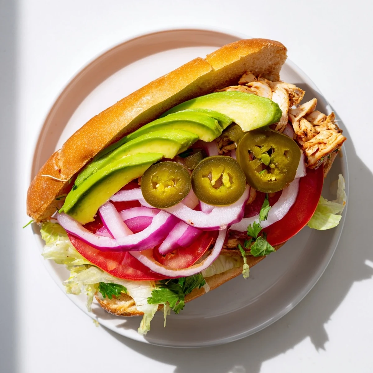 Hearty Chicken Torta Sandwich piled with sliced chicken, creamy avocado, and crisp vegetables on toasted bolillo roll