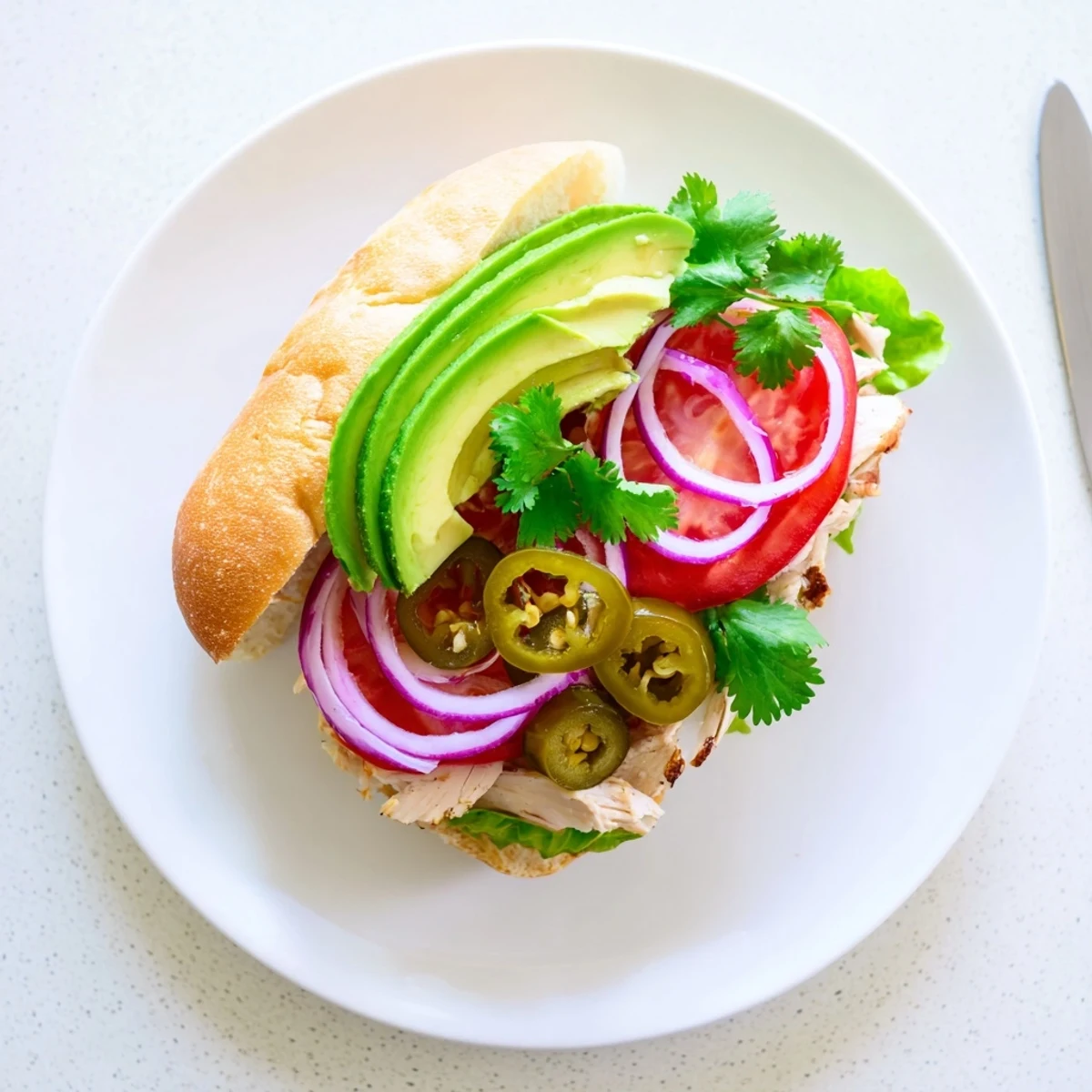 Cross-section of Chicken Torta Sandwich showcasing marinated chicken, ripe avocado slices, lettuce, and jalapeños on a split roll