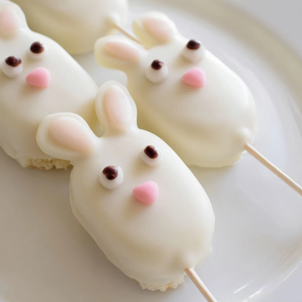 Adorable white chocolate bunny cakesicles with candy eyes on a festive Easter dessert platter