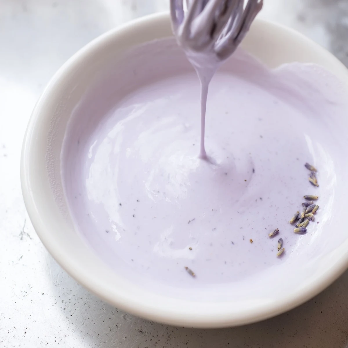 Smooth lavender glaze cascading down a golden pound cake slice on white ceramic plate