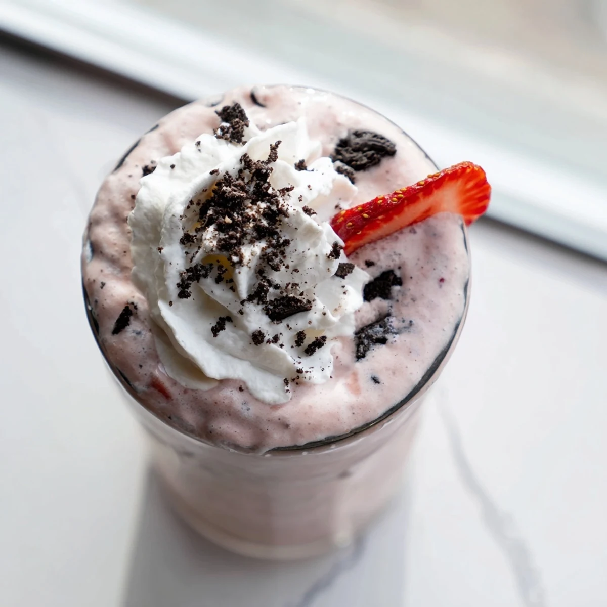 Thick pink strawberry Oreo milkshake topped with whipped cream and cookie crumbs in a chilled glass