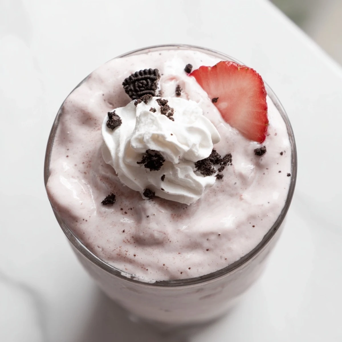 Two glasses of rich strawberry Oreo milkshake garnished with fresh strawberries and a fluffy whipped topping