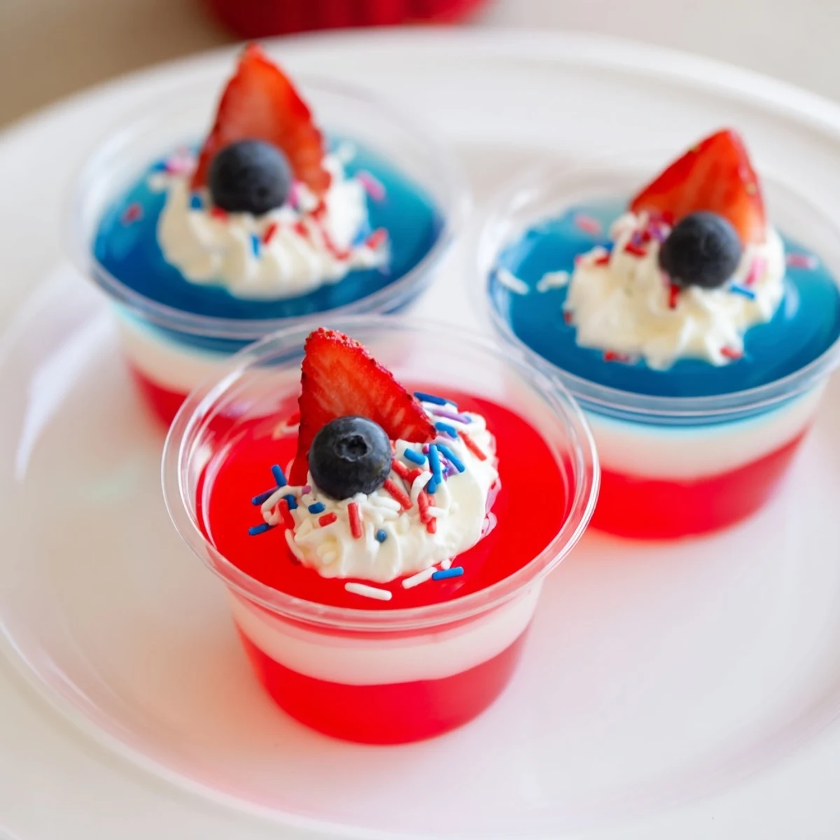 Bright Red White And Blue Jello Cups wobbling in clear cups, berry garnish.