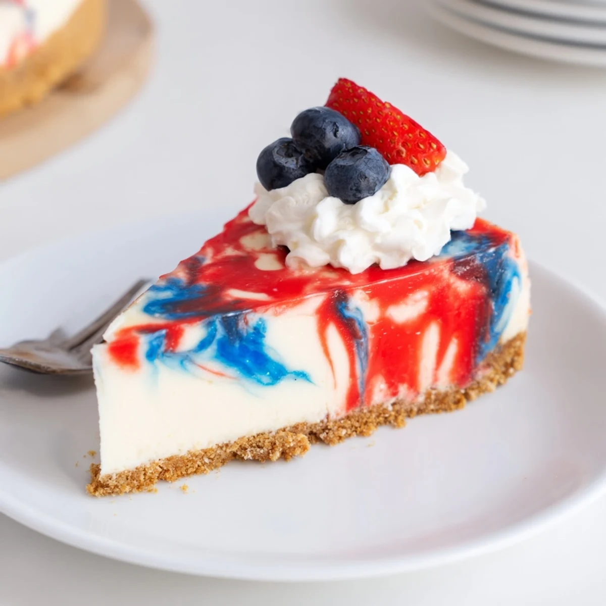 Slice of Patriotic Swirl Cheesecake topped with whipped cream and fresh berries