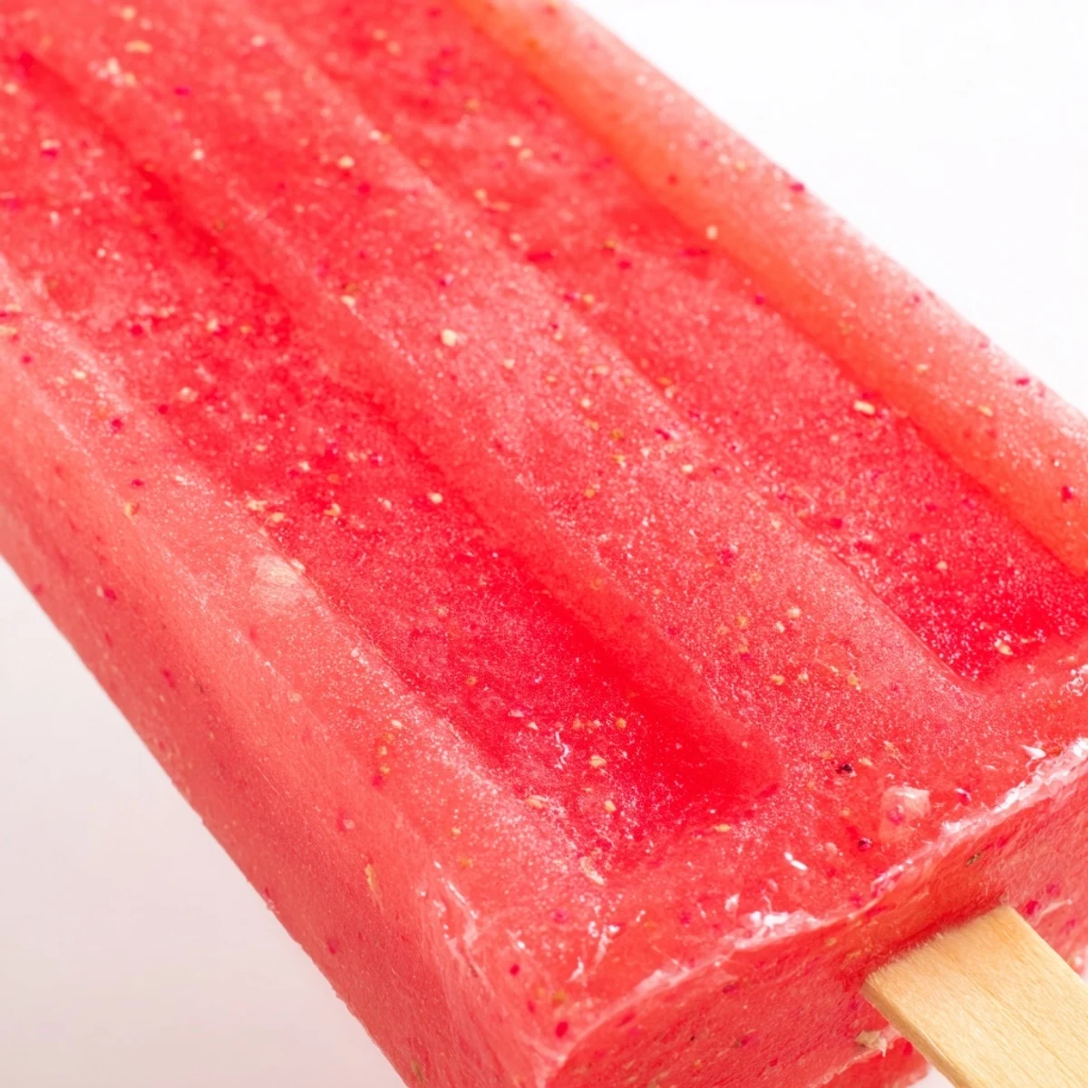 Three strawberry watermelon popsicles arranged on white plate with garnish of mint leaves and whole fresh strawberries