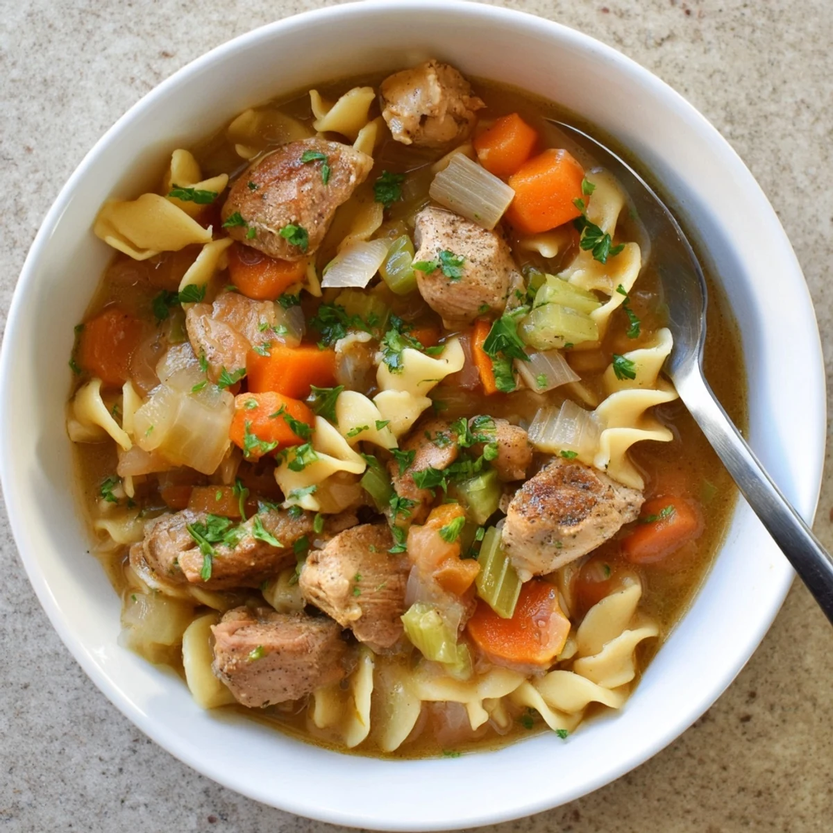 Steaming bowl of one pot chicken and noodles with tender meat and vegetables in golden broth.
