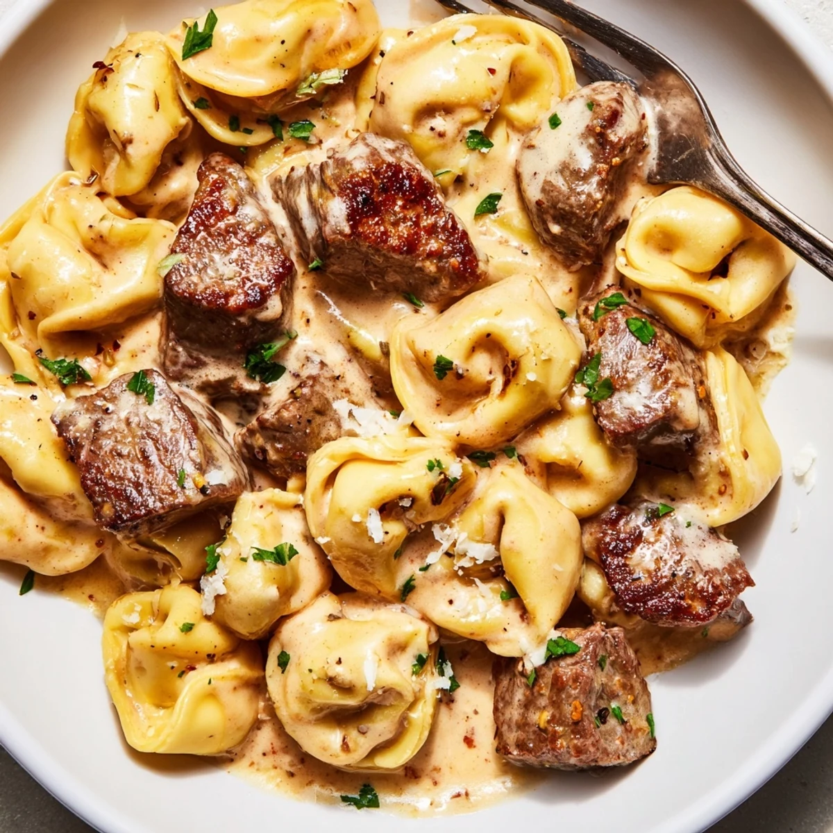 Steaming bowl of garlic steak tortellini with juicy sirloin pieces and rich creamy sauce