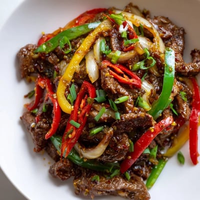 A close-up of a wok with caramelized beef, crisp peppers, and chilies, served with jasmine rice for an easy weeknight Spicy Beef and Pepper Stir Fry.
