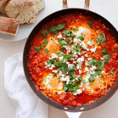 Brightly colored Quick Shakshuka Eggs simmering in a spiced tomato sauce, garnished with fresh cilantro and crumbled feta cheese on top.