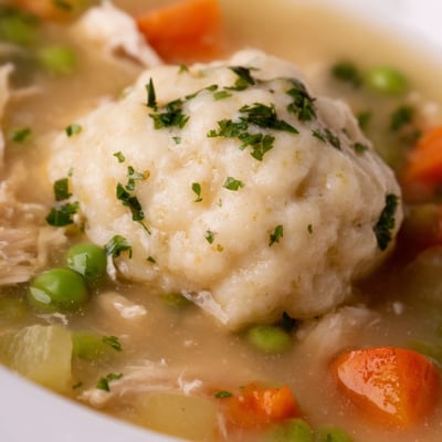 One Pot Chicken Dumpling Soup shows hearty chicken, carrots, and onions in a ladleful of steamy broth.